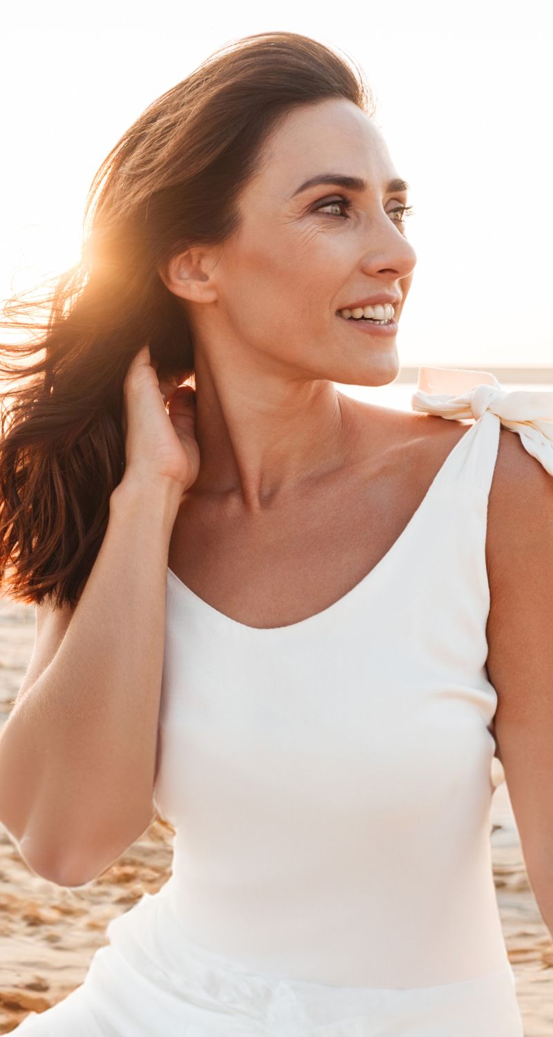 Woman smiling in a sunlit beach setting.