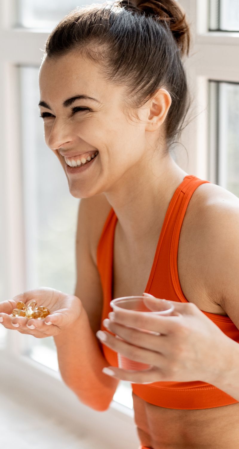 Smiling woman holding vitamins and a drink.