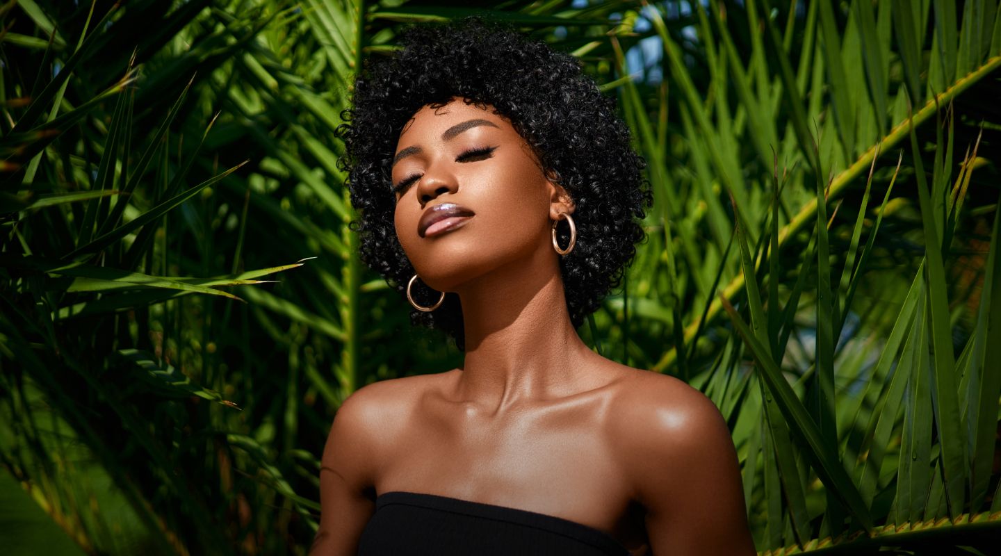 Woman with curly hair enjoying sunlight outdoors.