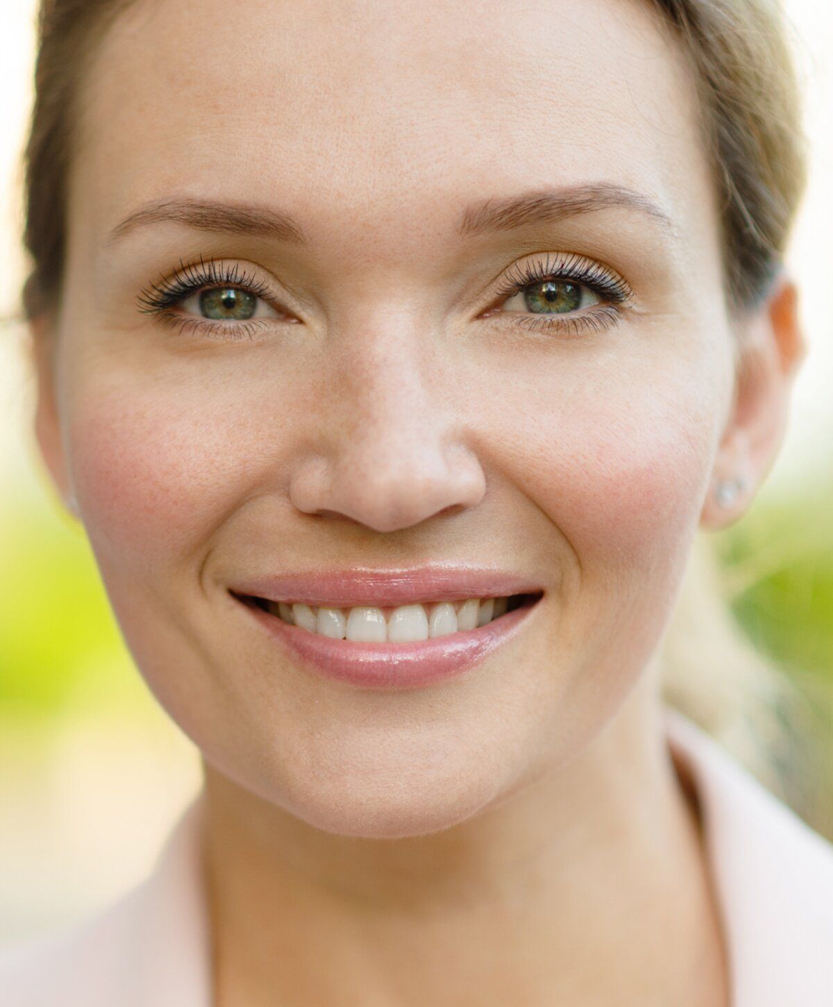 Smiling upneeq patient model with green eyes outdoors.