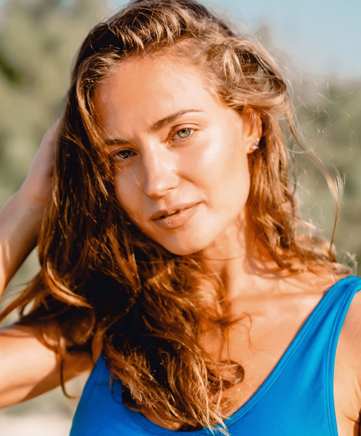 botox patient model with wavy hair in blue swimsuit outdoors.