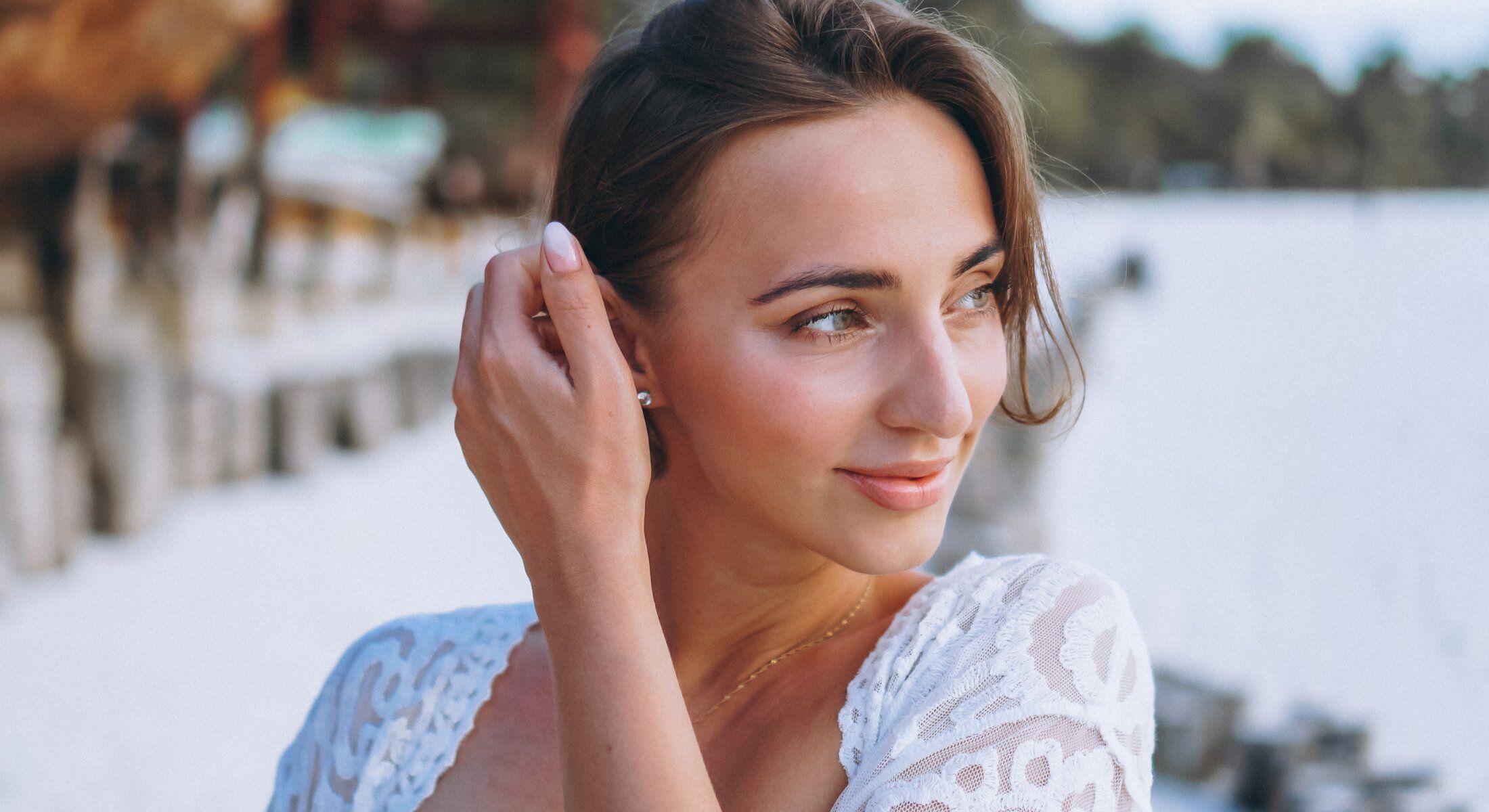 Young injectables & fillers patient model touching her hair at the beach.