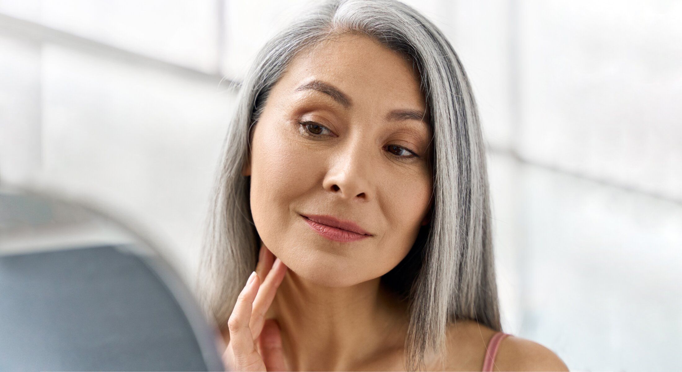 Wrinkle treatment patient model with gray hair examining her reflection.