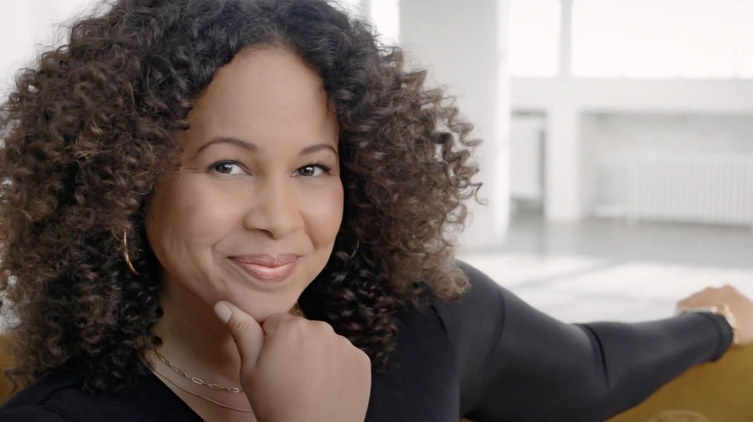 Smiling woman with curly hair, thoughtful expression.