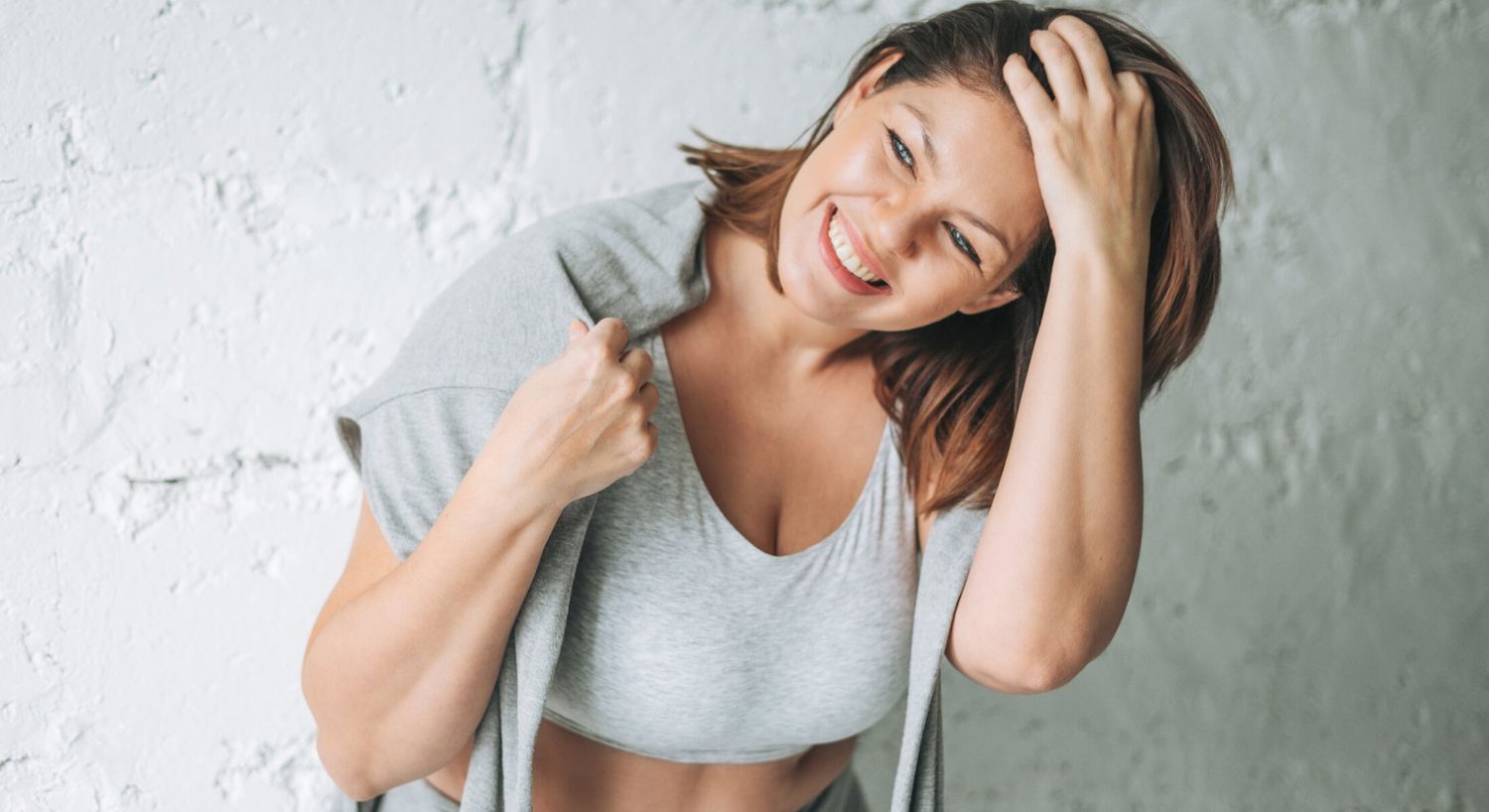 High Dose Vitamin C IV therapy patient model in gray athletic attire laughing and running her fingers through her hair